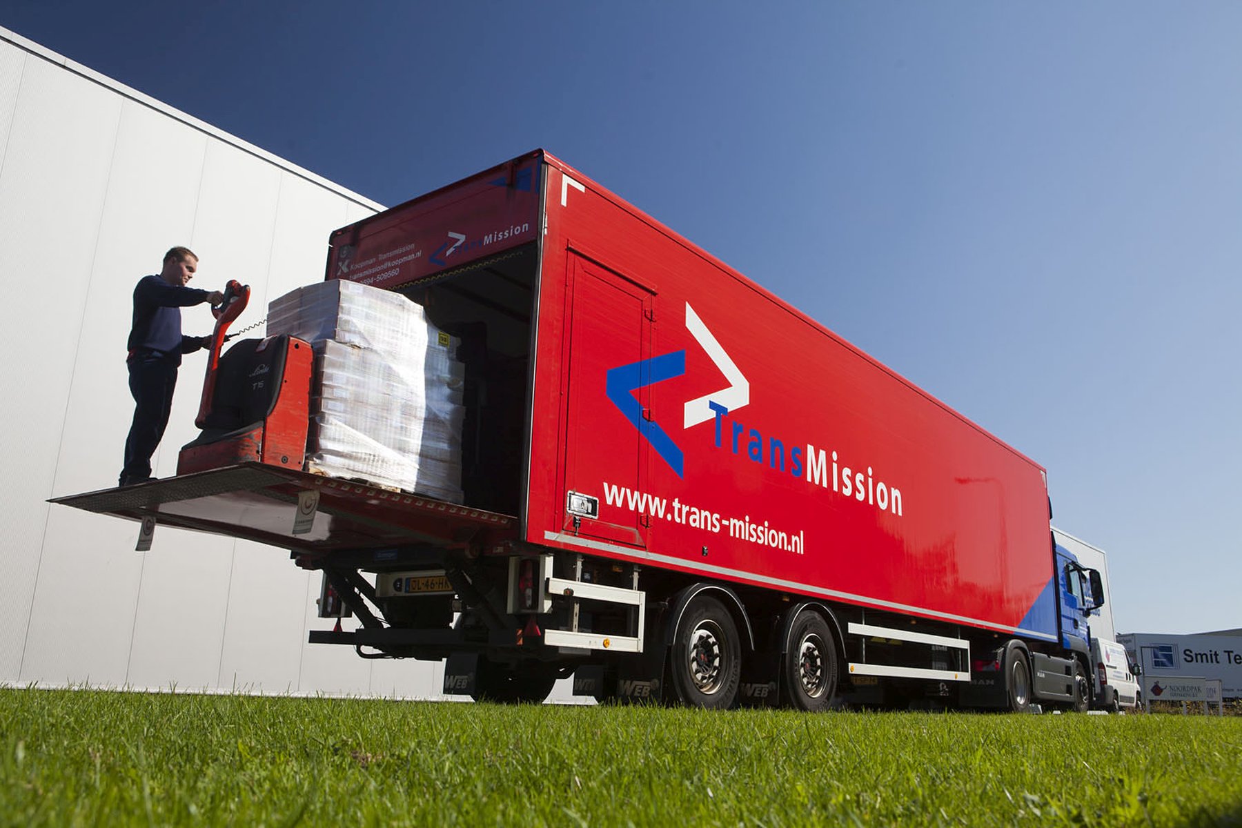 TransMission-medewerker laadt zendingen bij een rode distributievrachtwagen